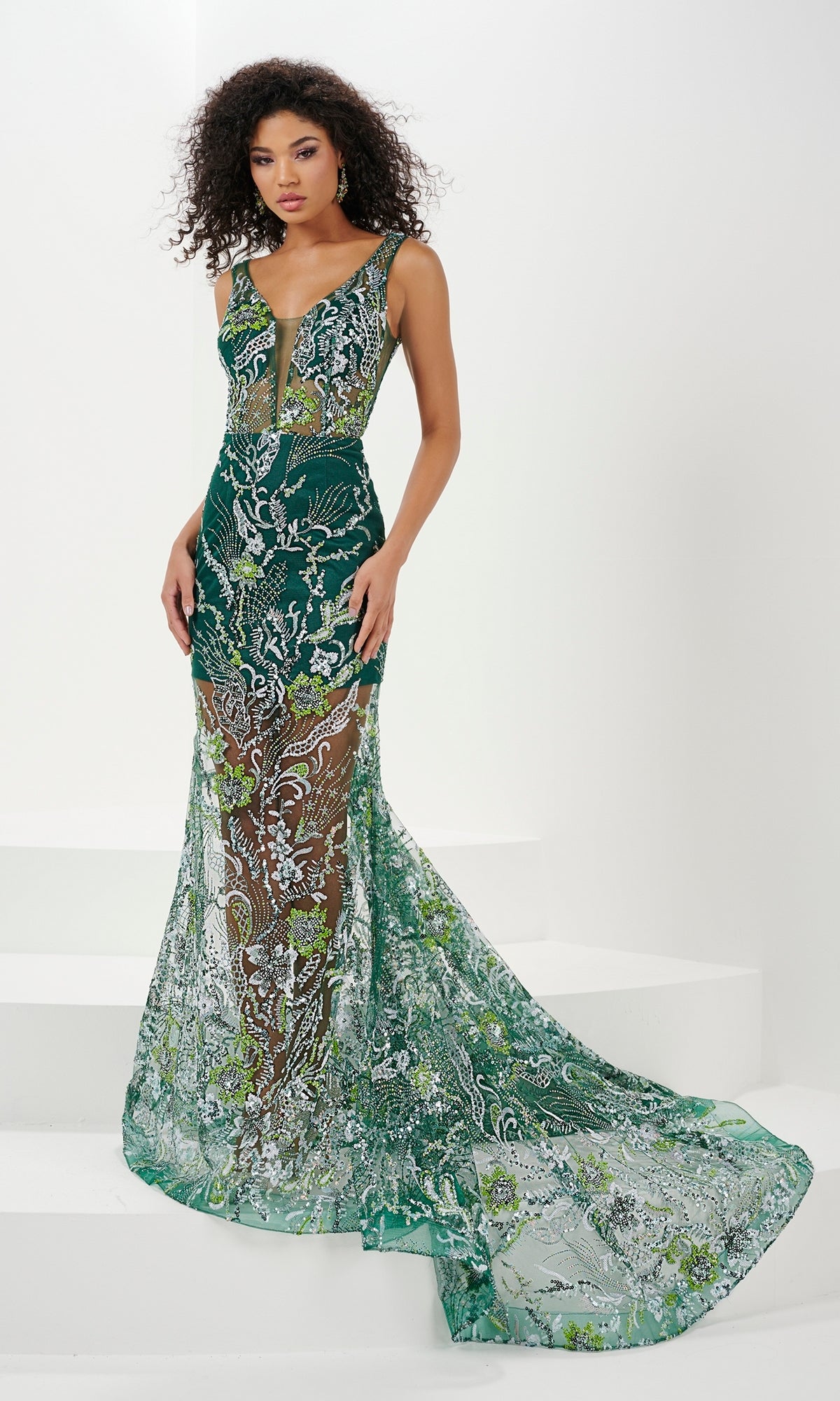 A woman stands gracefully on white stairs in a Mini Sequin Prom Dress with a sheer long overlay, featuring intricate silver and green embroidery and floral sequin designs.
